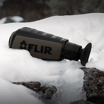 Teledyne FLIR Scout III handheld thermal monocular seen siting on a snow covered rock.