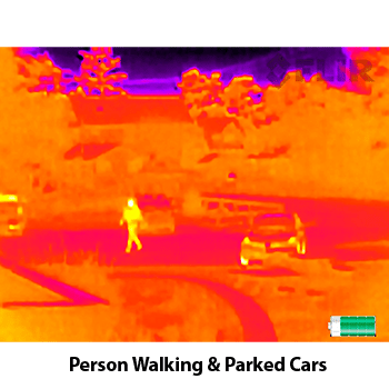 Thermal image of a person walking by parked cars.