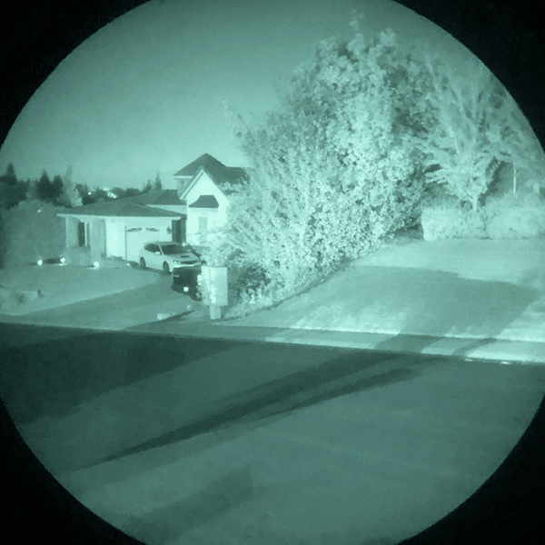 Looking through the lens of a AN/PVS-14A GEN III unit you can see a neighborhood at night.