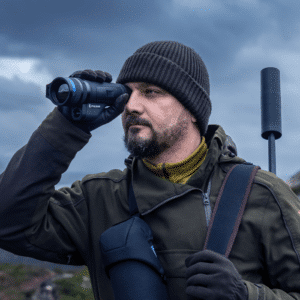 Man in cold weather hunting gear shown looking through the lens of a Pulsar Telos LRF XP50 thermal monocular.