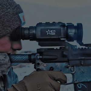 Photo of a man looking through the lens of an AGM Rattler V2 thermal rifle scope mounted to an AR15 rifle.