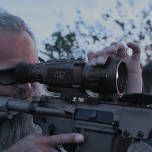 Man shown looking through the lens of an AGM Clarion dual focus thermal weapon sight mounted to an AR15 style rifle.
